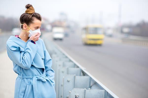 Femme au bord de la route portant un masque anti-pollution