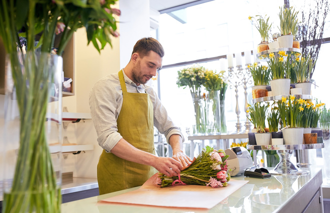 Adulte fleuriste en reconversion entrain d'emballer un bouquet pour un client