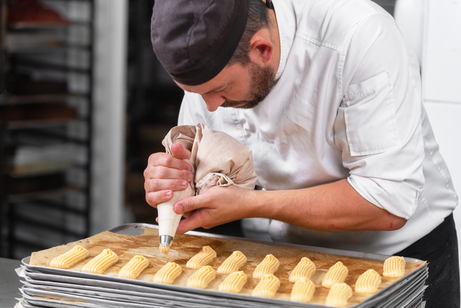 Dressage d'éclairs au chocolat par un pâtissier avec une poche à douille