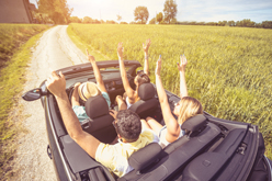 Plusieurs jeunes dans une voiture les bras levés vers le ciel.